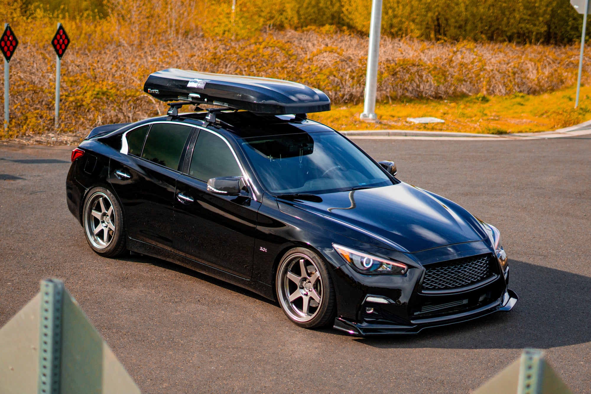 Black INFINITI Q50 car with a roof box parked on a road