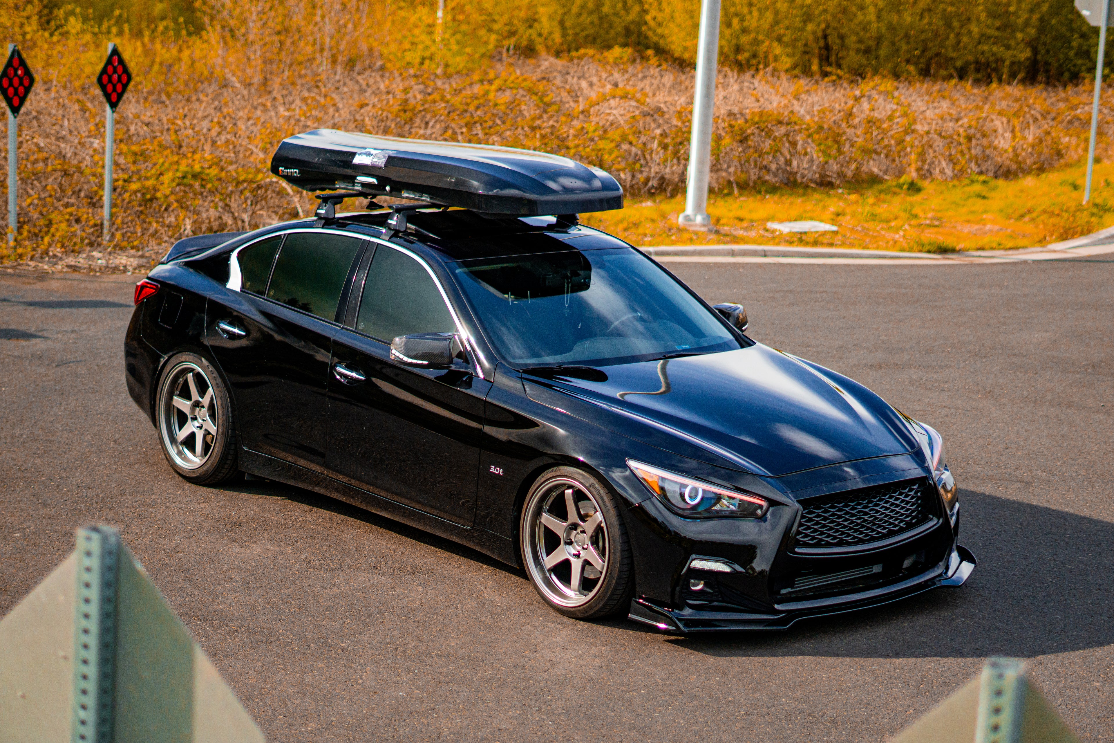 Black INFINITI Q50 car with a roof box parked on a road